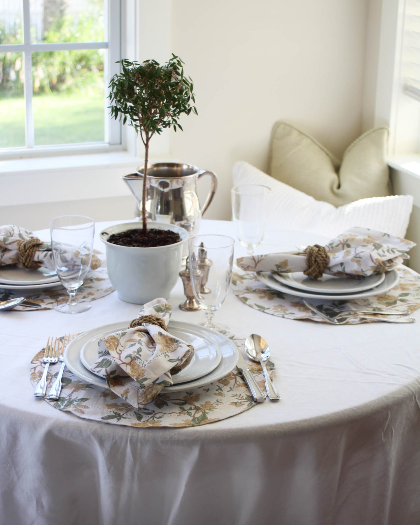 Elegant table setting with white tablecloth, yellow floral round placemats, and matching napkins.