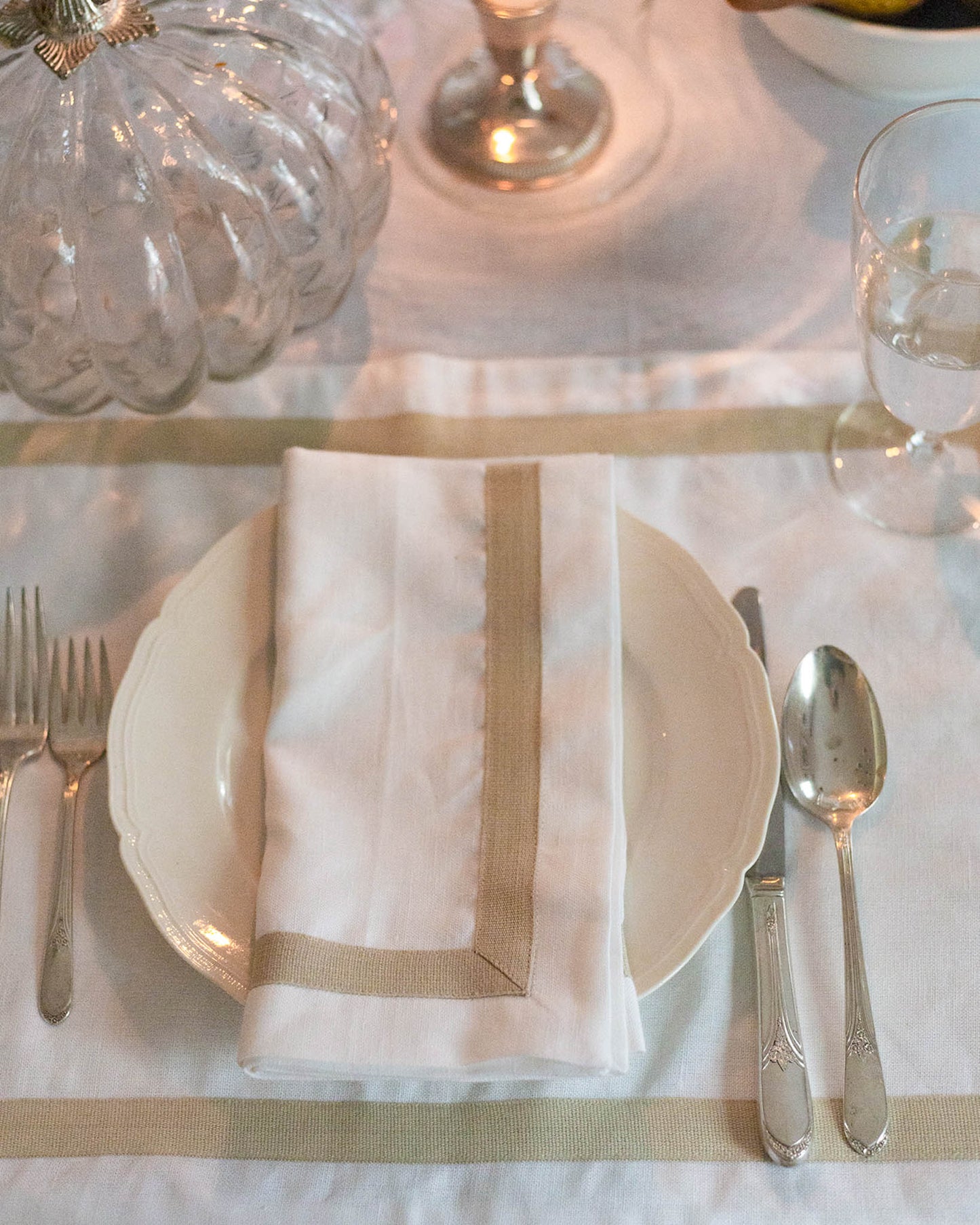 Elegant table setting with white plates, silverware, and a folded napkin on a white tablecloth.