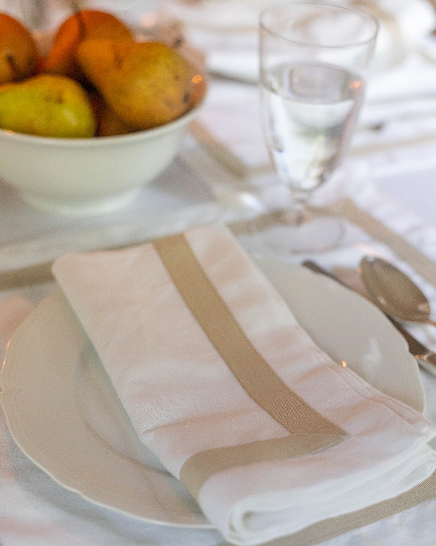 Elegant holiday table setting with a white plate, striped napkin, and fruit bowl.
