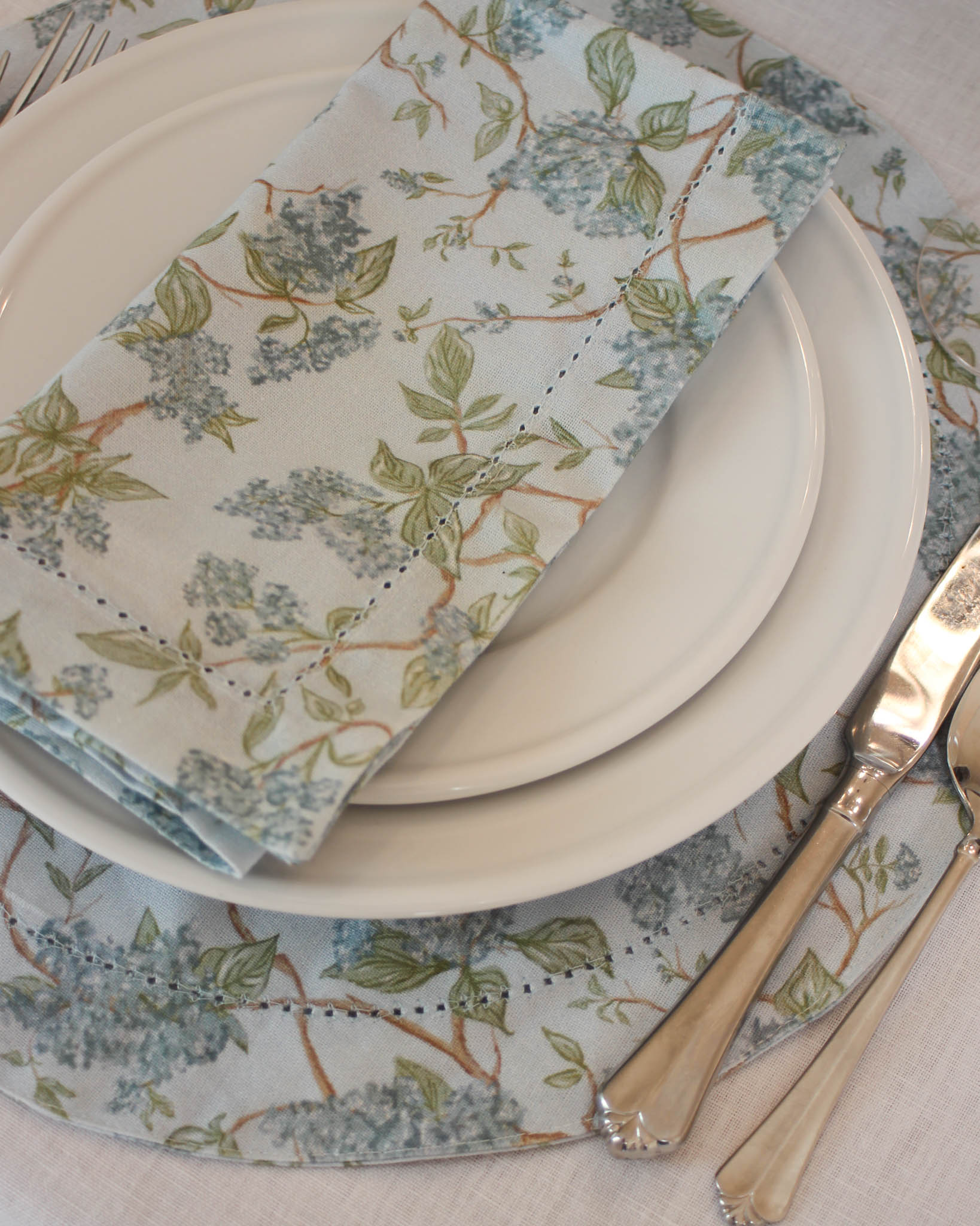 Festive holiday table decor with blue floral dinner napkins and matching placemats  with hemstitch detailing