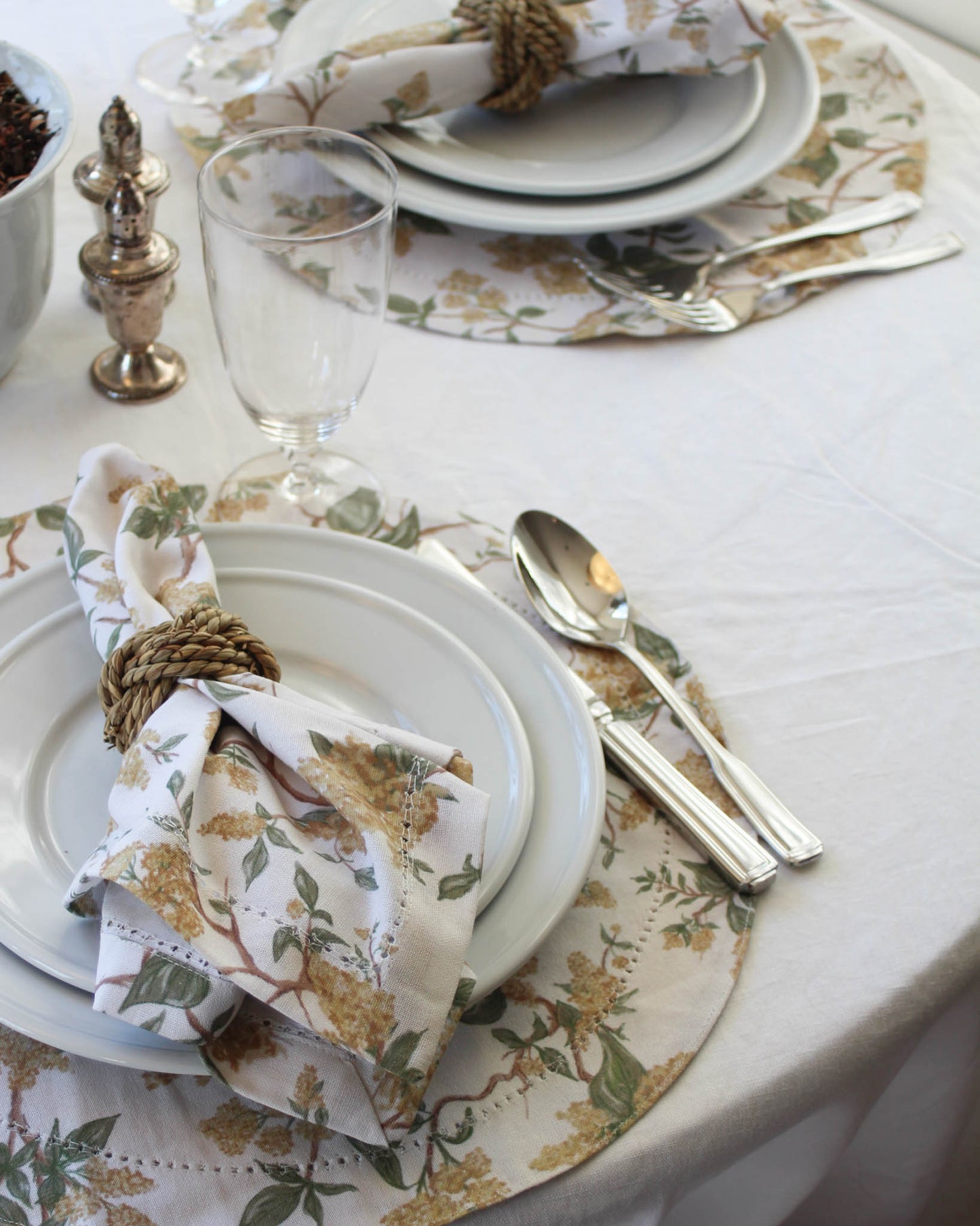 Elegant table setting with yellow floral napkins, silverware, and glass on a white tablecloth.