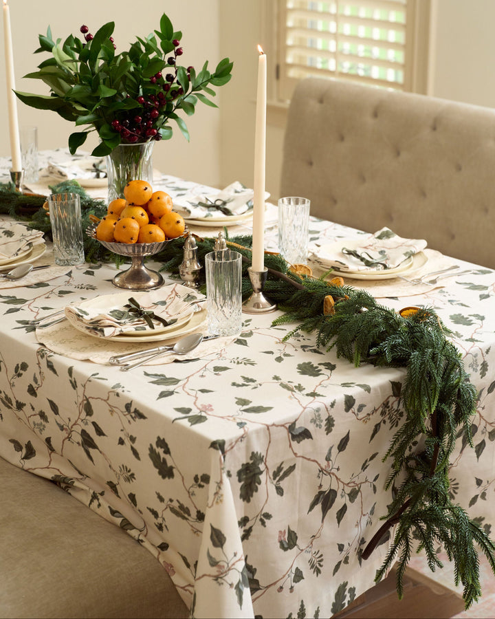 English countryside Christmas table with a neutral botanical tablecloth, oak leaves, winter greenery, cut crystal, and classic holiday decor.