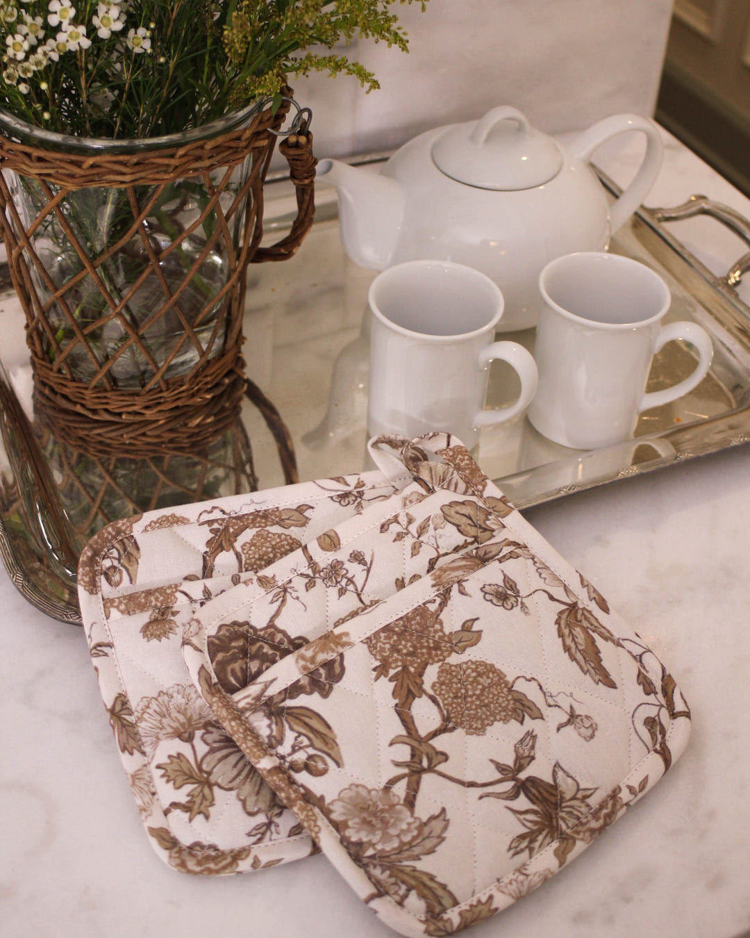 A set of two chestnut brown floral potholders with a vintage botanical print, perfect for grand millennial decor. These 8 inch square quilted potholders for baking and cooking are made from premium cotton with thick recycled cotton insulation for safe handling of hot dishes and pans. Each woven potholder features a convenient hanging loop. Use them as quilted hot pads or floral hot pads to protect surfaces during Easter baking or a Mother's Day brunch. A great gift for mom or grandma gift.