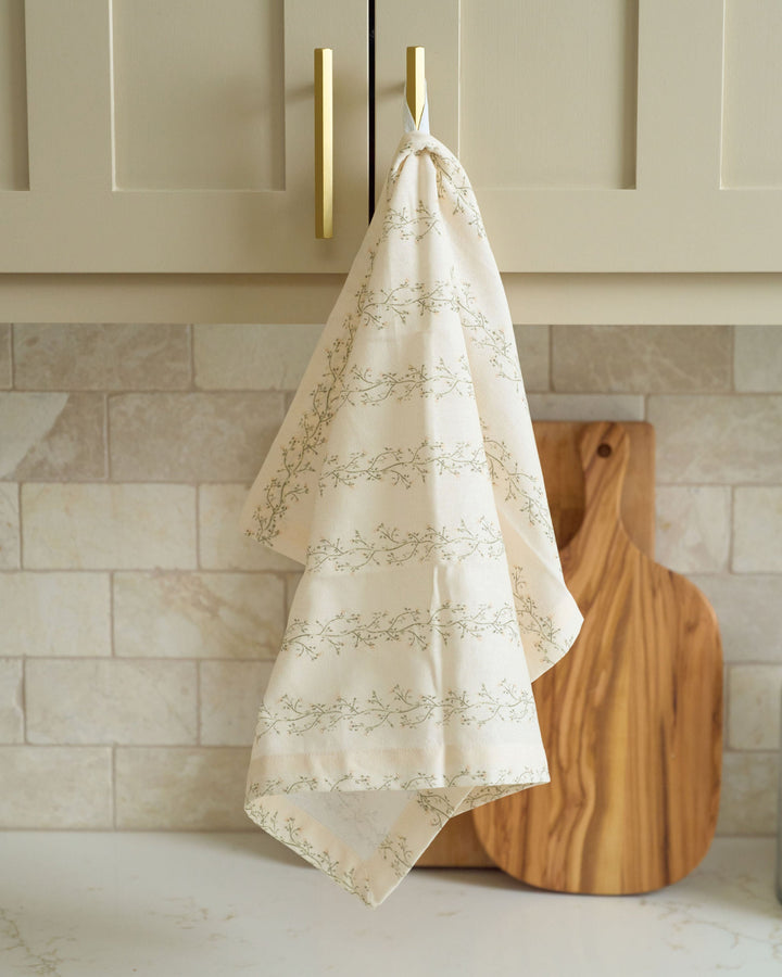 Cream floral stripe cotton tea towel featuring hand-drawn moss green and pale yellow botanicals, styled for everyday kitchens, spring brunches, summer hosting, fall cooking, Thanksgiving preparations, Christmas baking, holiday décor, hostess gifting, and year-round display.