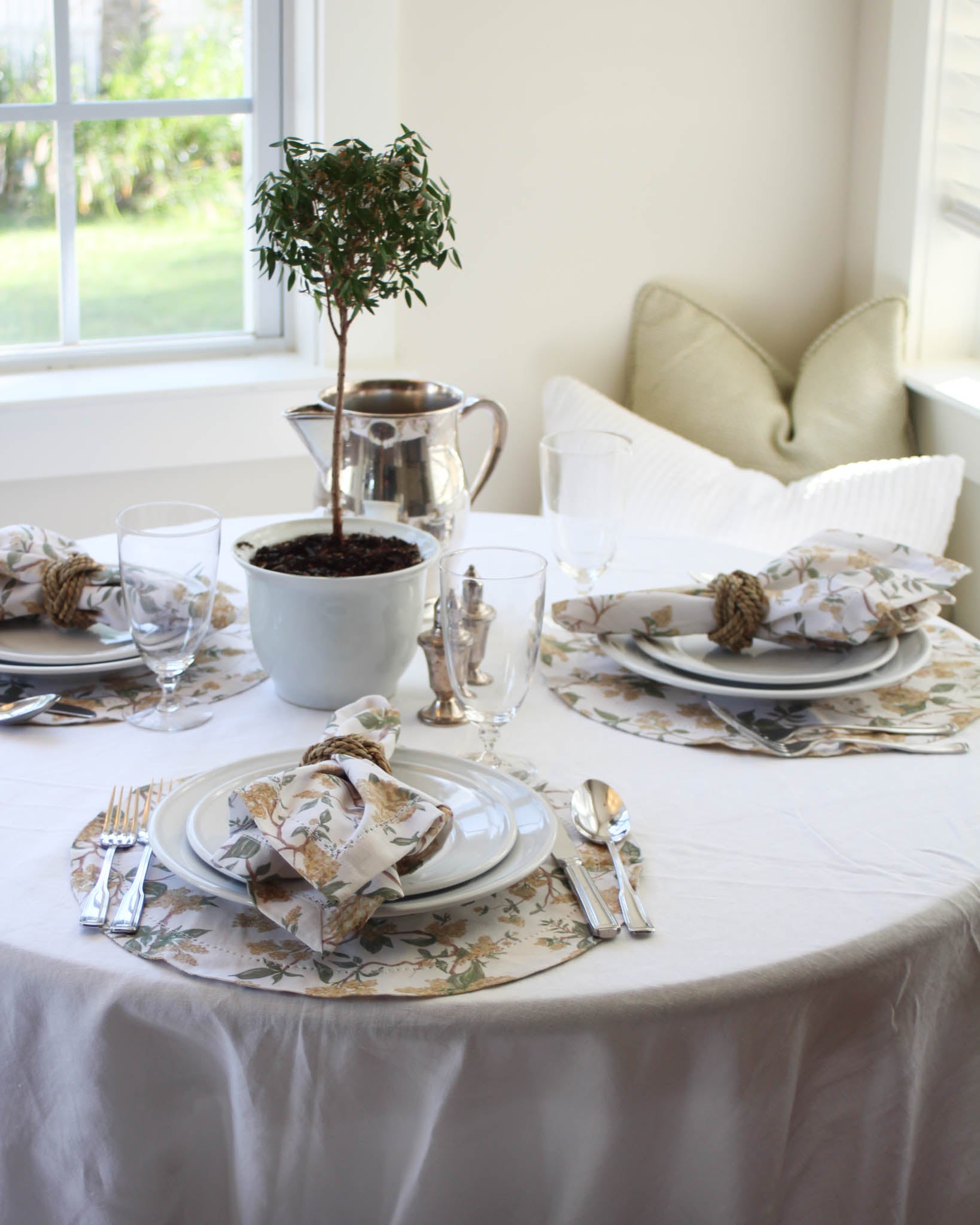 Elegant table setting with white tablecloth, yellow floral round placemats, and matching napkins.