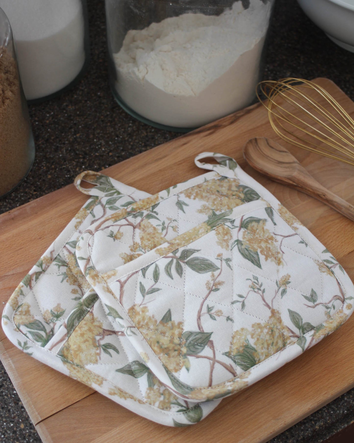 Floral patterned pot holder on a wooden cutting board with kitchen items in the background.