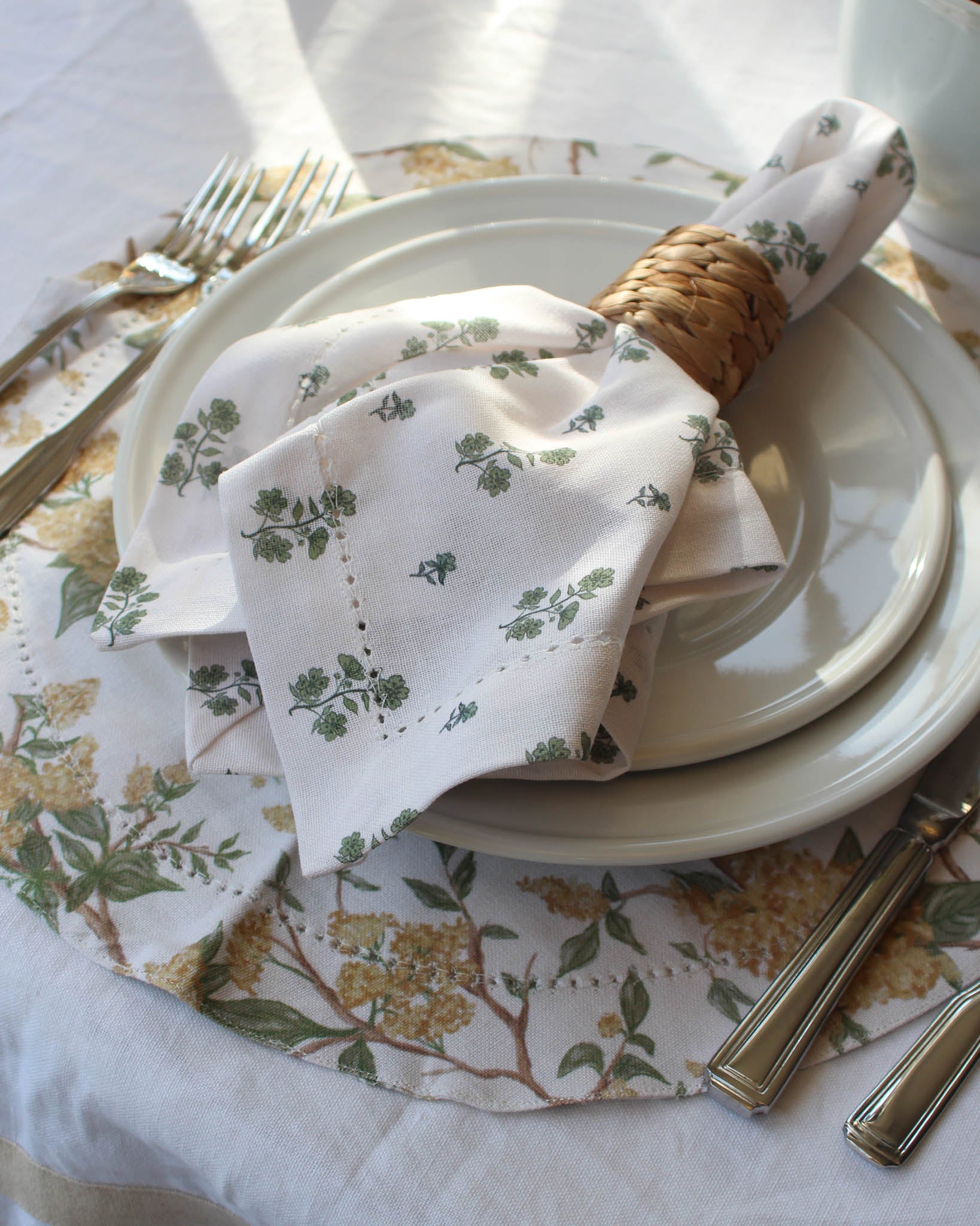 Set table with green floral napkin, plates, and cutlery on a patterned tablecloth.