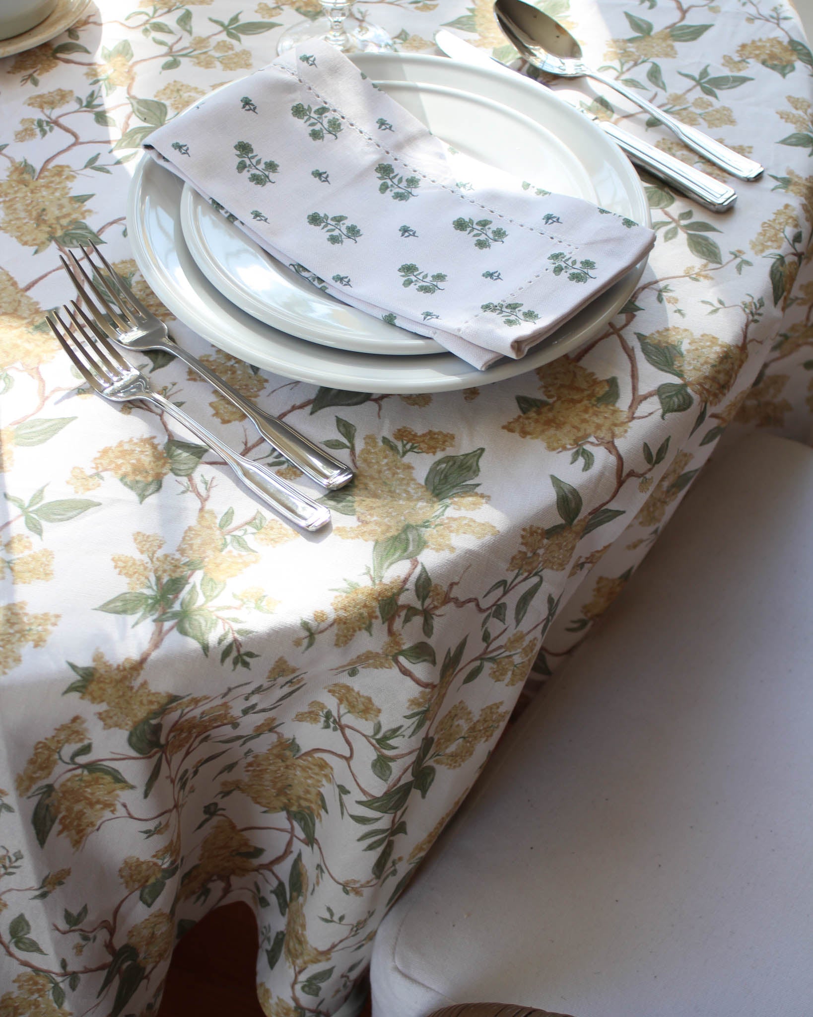 Set table with yellow floral-patterned tablecloth, plates, and cutlery.