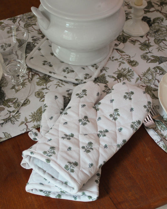 Folded floral-patterned oven mitts on a wooden table with a floral table runner