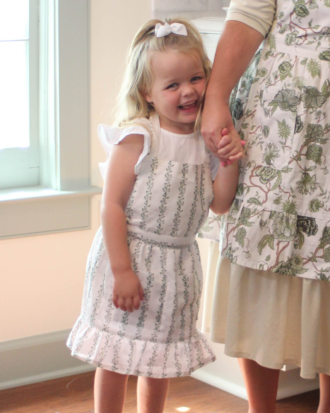 Kids stripe apron in cotton with ruffle hem, gathered waist, and front pockets for holiday cooking and baking.