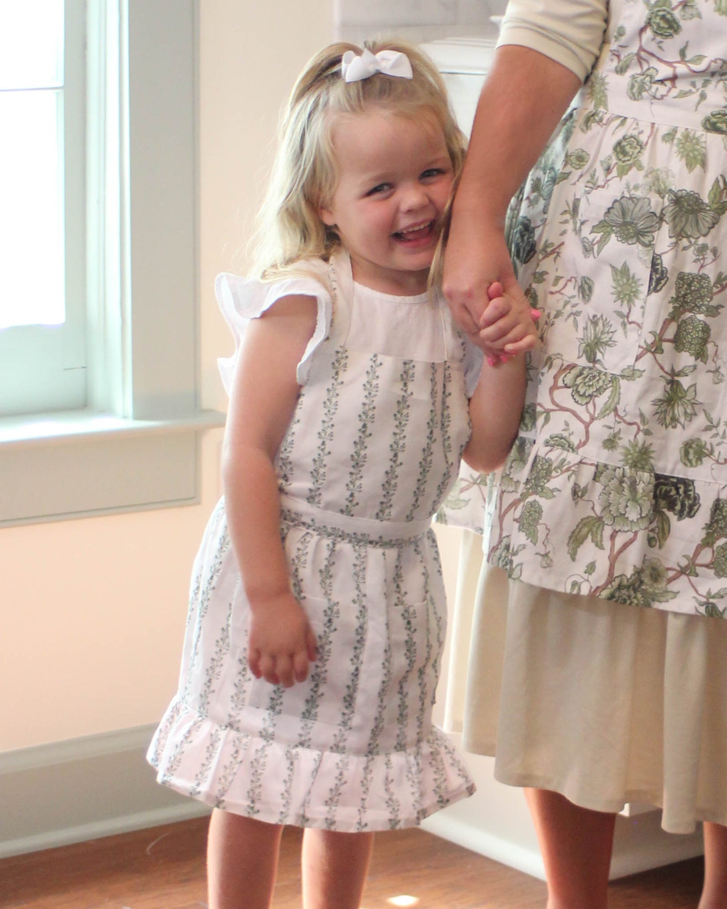 Kids stripe apron in organic cotton with ruffle hem, gathered waist, and front pockets for holiday cooking and baking.