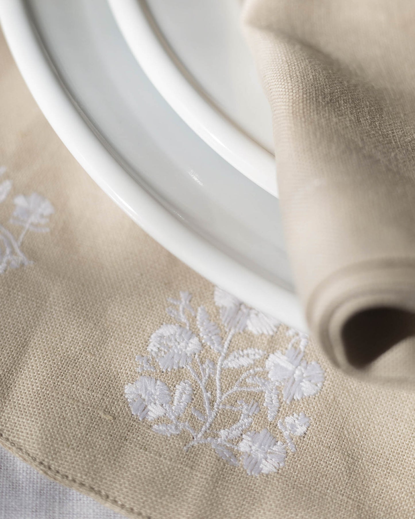 This set of 4 round placemats, crafted in a soft neutral beige with intricate white floral embroidery, brings a timeless elegance to your table. 