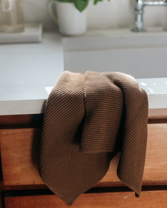 Close-up of a soft beige knitted towel featuring an elegant white monogram surrounded by a floral border. This organic cotton towel is reusable and perfect for kitchen, bathroom, or hand and face drying.
