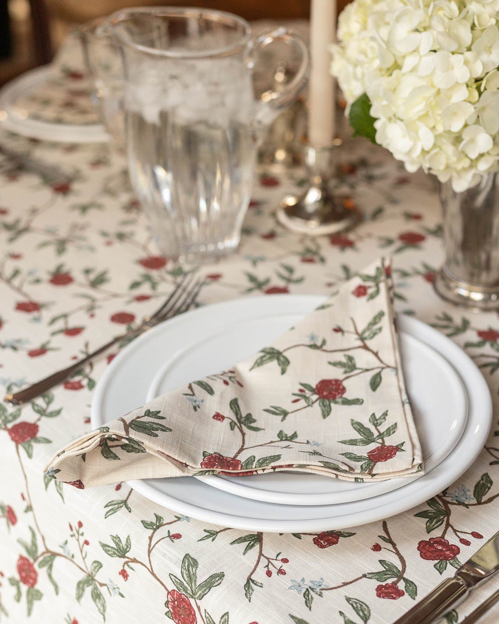 Set table with floral tablecloth, plates, and a napkin with a red and green pattern.