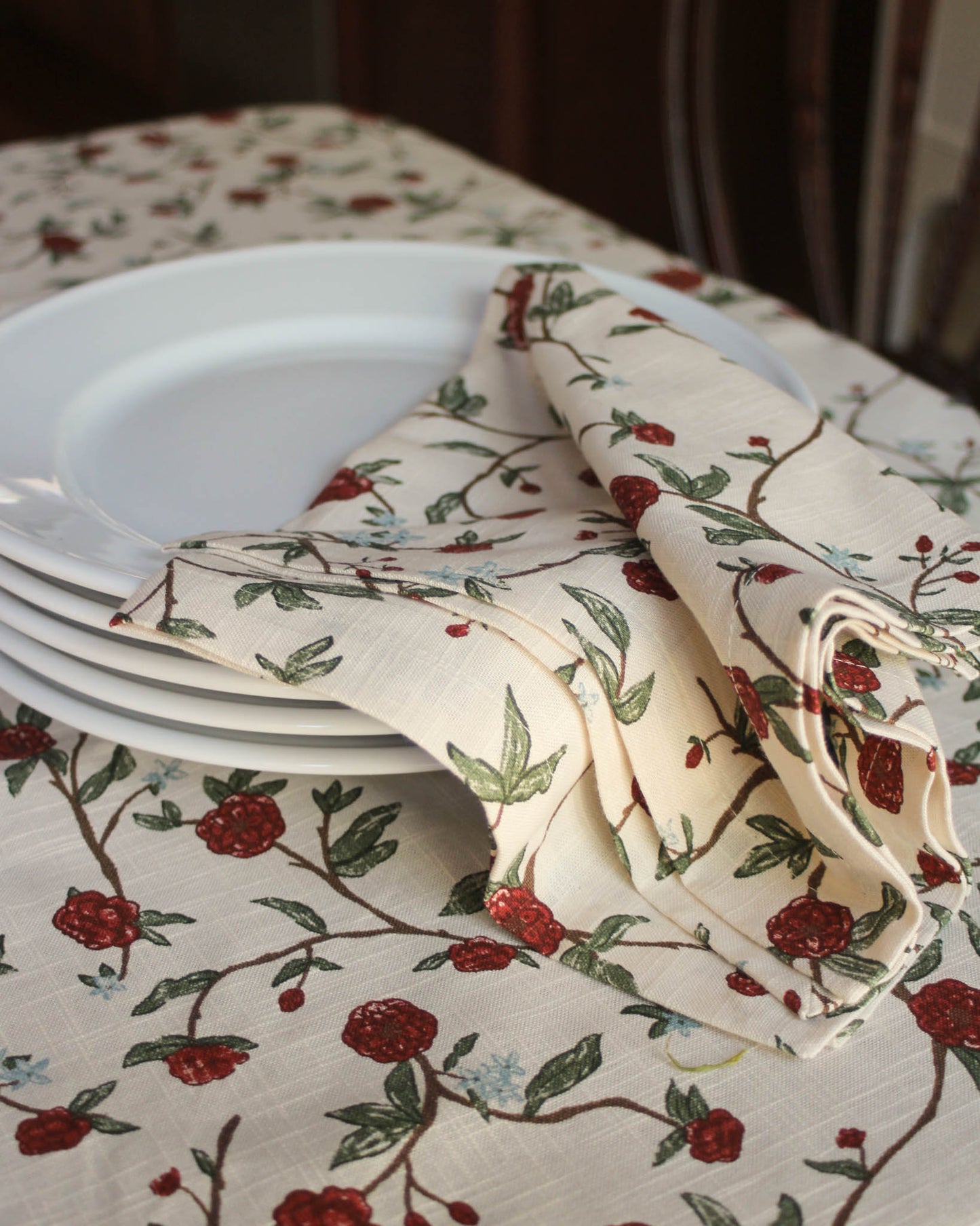 Stack of white plates on a floral tablecloth with red flowers and green leaves.