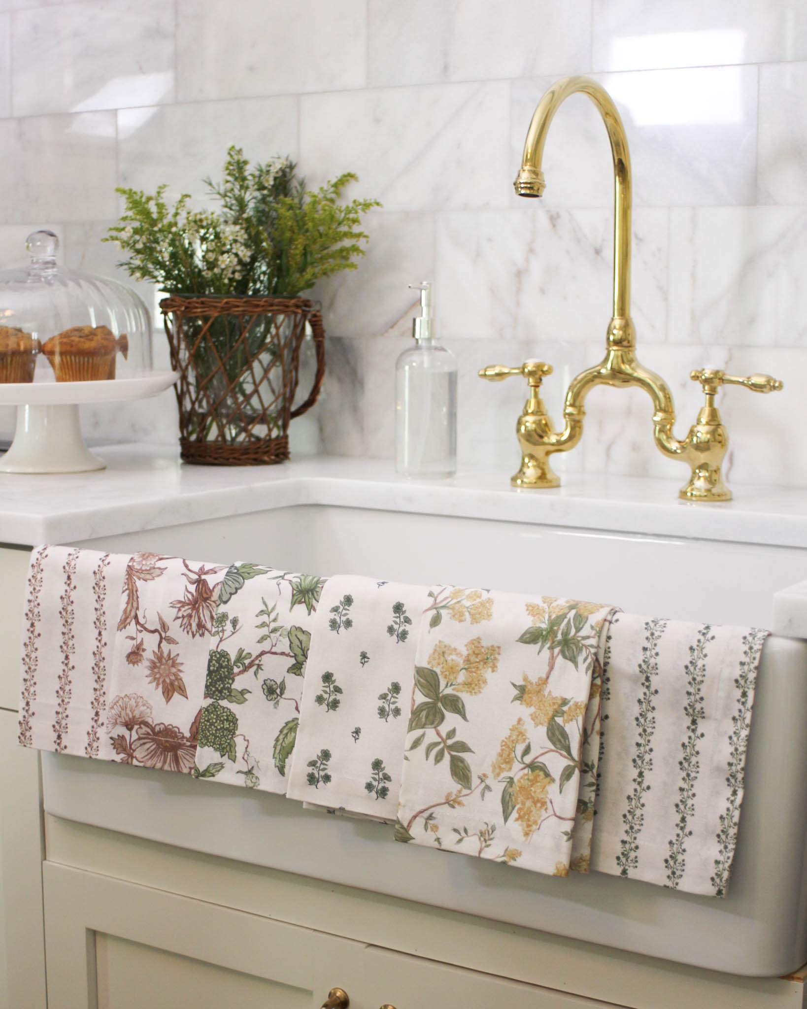Floral tea towels hanging over a kitchen sink with a gold faucet. A collection perfect for holiday hosting and gifting 