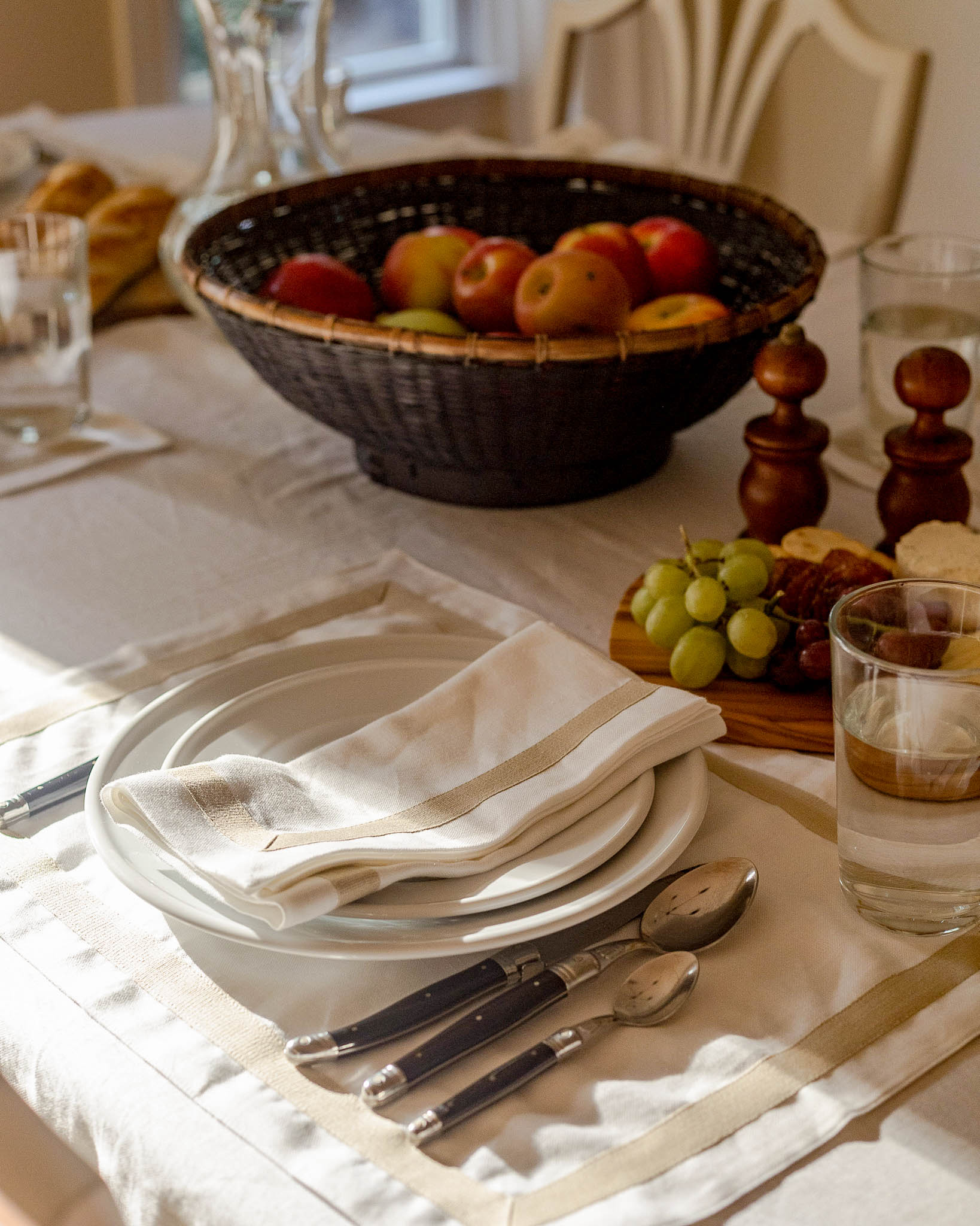 Dining table setting with a bowl of fruit, plates, and cutlery on a white tablecloth. Perfect for Fall tablescapes, Thanksgiving table decor, and entertaining.