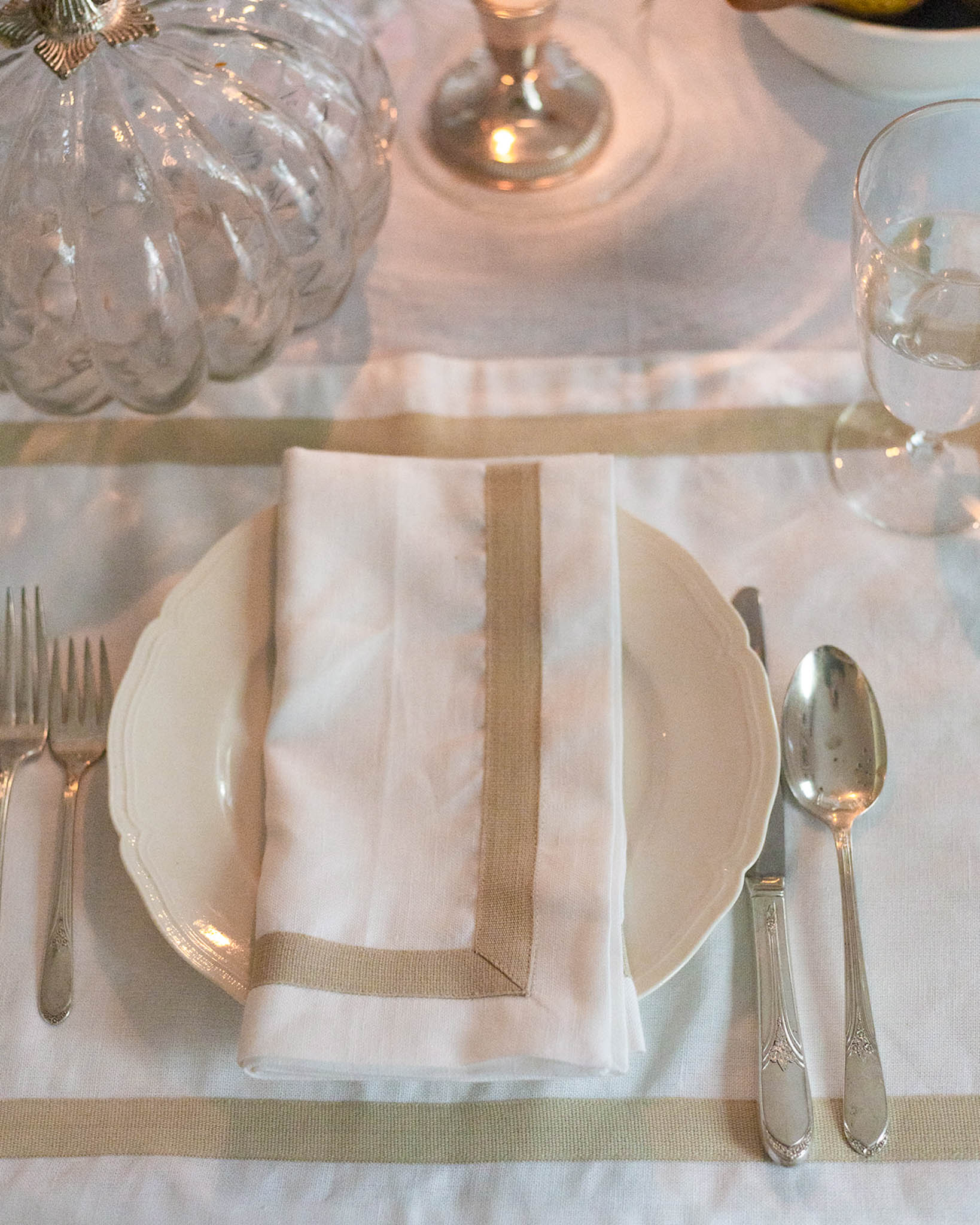 Elegant table setting with white plates, silverware, and a folded napkin on a white tablecloth.