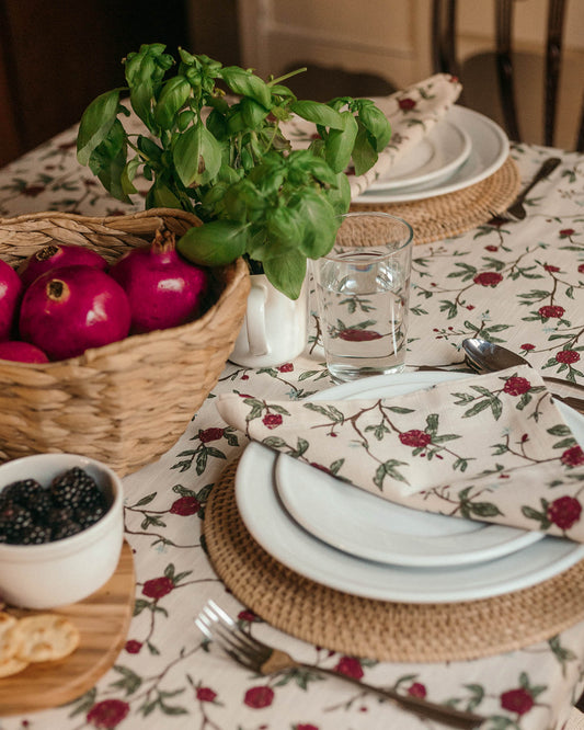 Dining table setting with floral tablecloth, plates, napkins, and a basket of pomegranates.
