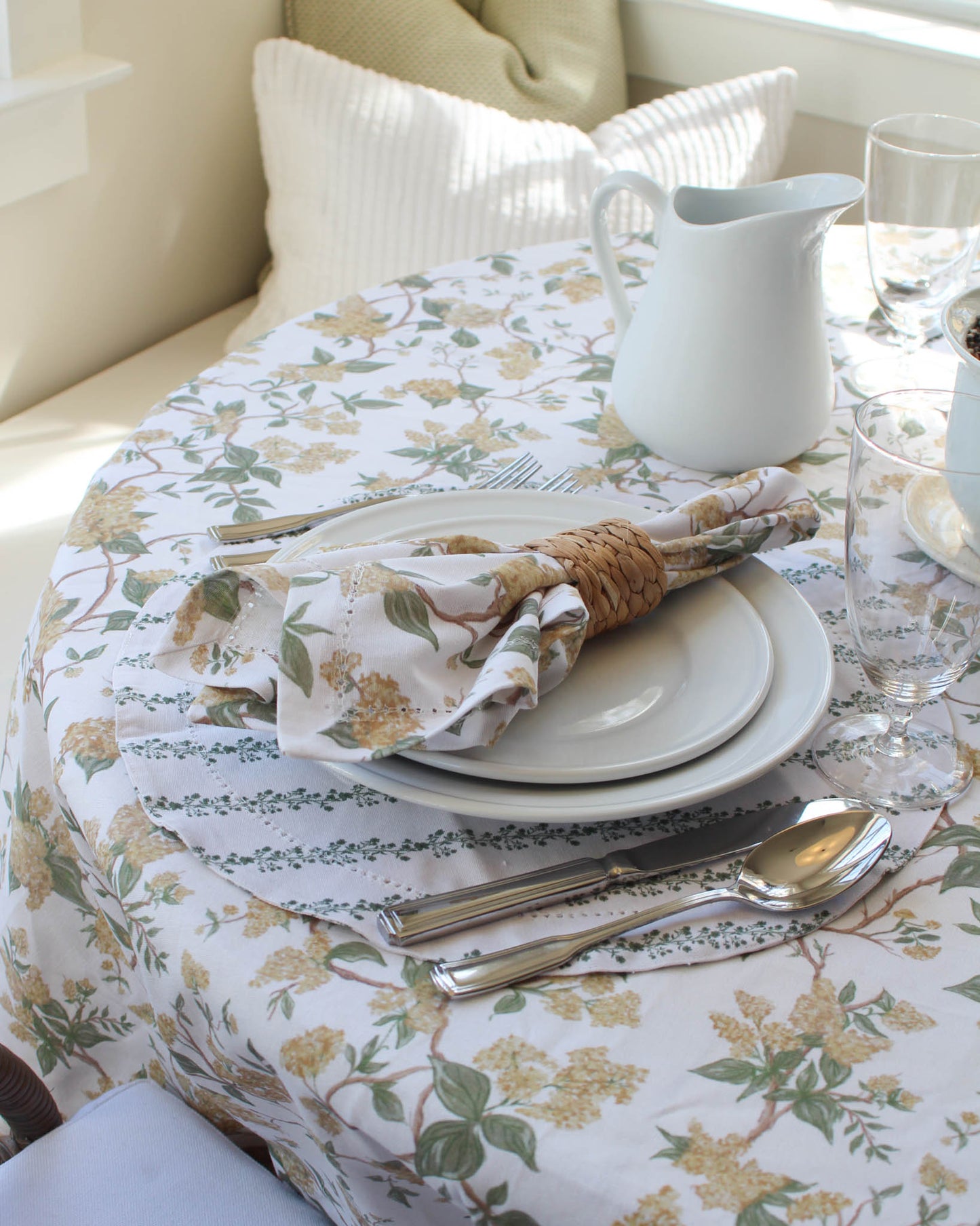 Set table with floral yellow tablecloth, plates, silverware, and a pitcher.