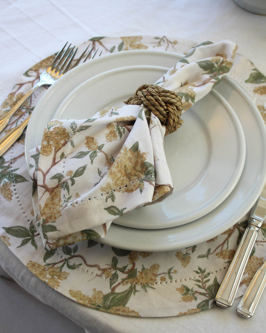 Set table with yellow floral napkin, plates, and cutlery on a matching round placemat.