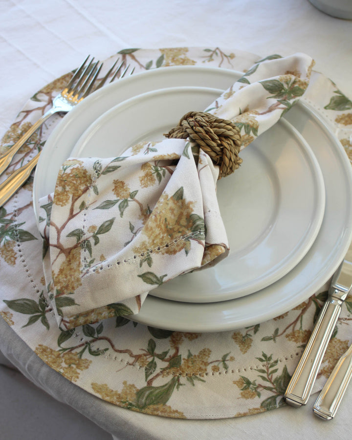 Brighten your holiday hosting with these yellow floral round placemats. Featuring a vibrant botanical print of sun-drenched flowers and leafy vines, these cloth placemats bring a joyful charm to your Easter table decor. The elegant hemstitched edge adds a clean, tailored finish to the design. Perfectly sized for spring dining, these washable cotton placemats pair beautifully with white scalloped china for a sophisticated, layered look that celebrates the arrival of the new season.