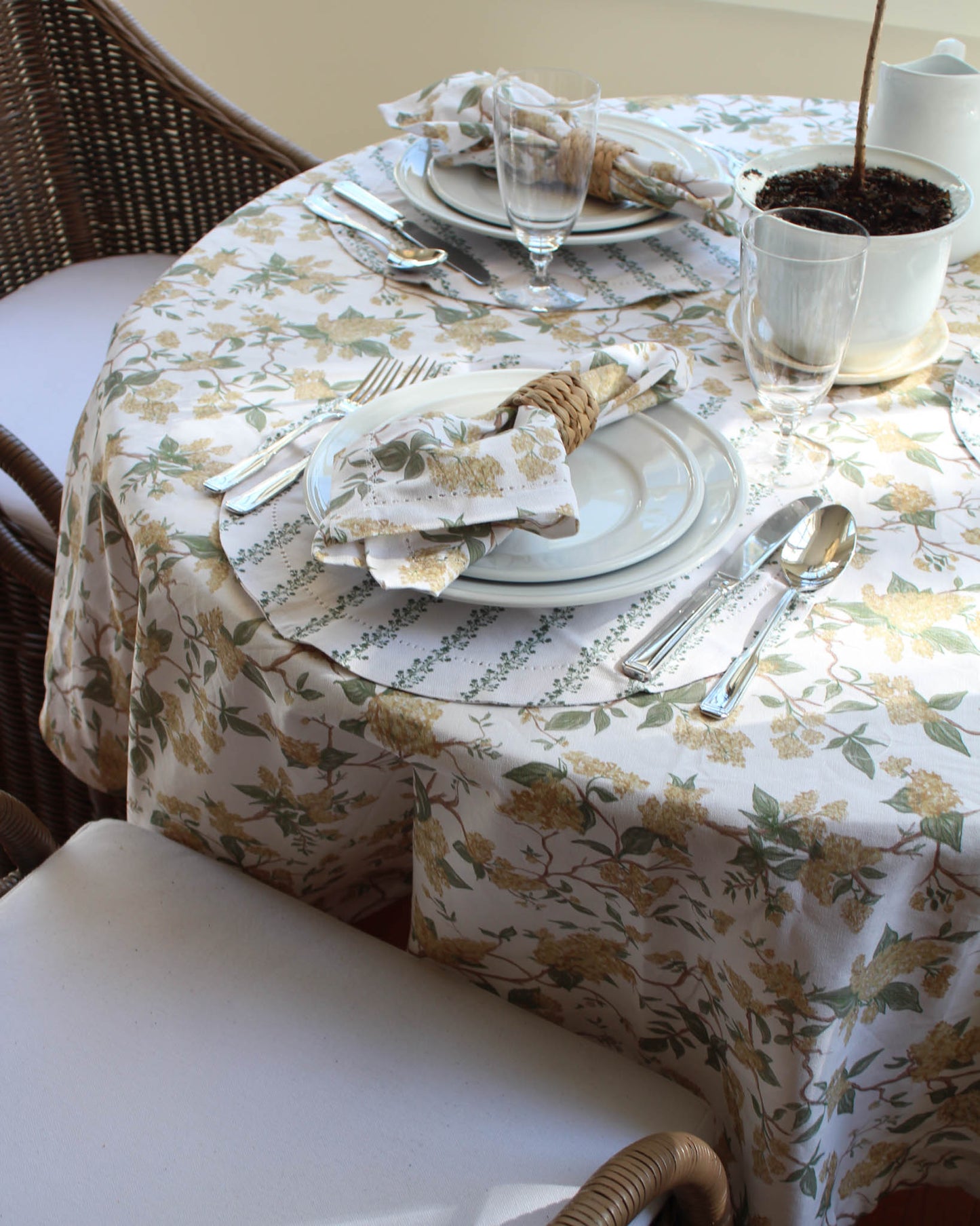 Dining table set with yellow floral tablecloth, plates, silverware, and glasses.