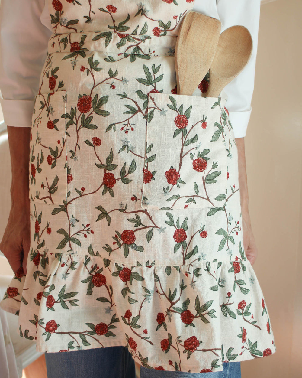 Elevate your country kitchen accessories with this red and green floral smock apron featuring a rich spring bouquet print. The 100% cotton fabric and ruffle hem create a stylish apron dress look, perfect for a Mother's Day gift for mom or a baker. This smock apron includes two pockets and adjustable ties, making it a versatile gardening apron or chef apron. Ideal for Easter baking and spring summer entertaining, it adds a touch of charm to every mother daughter kitchen moment.