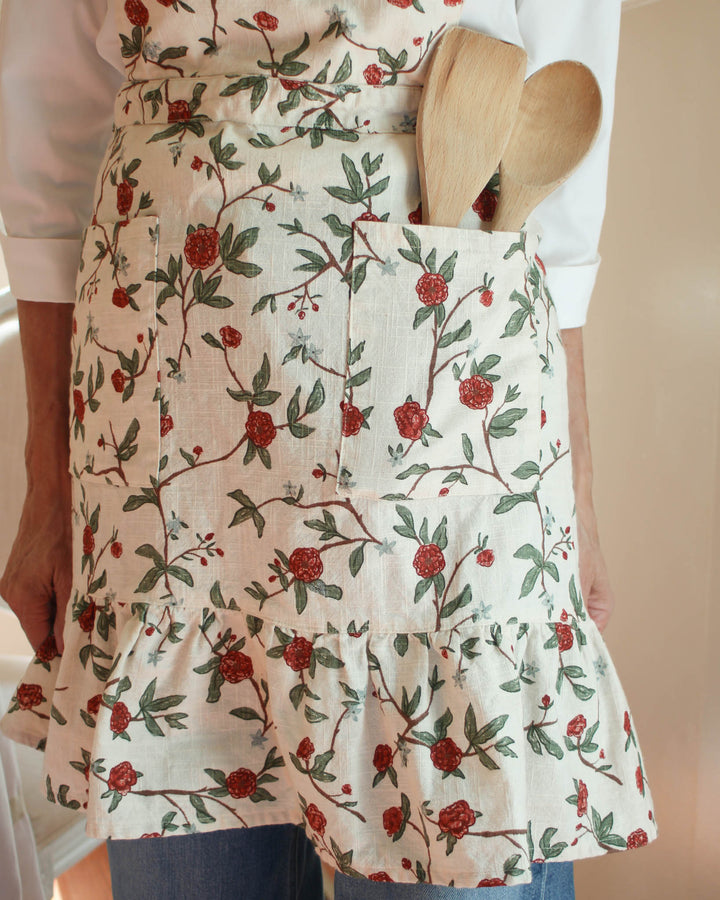 Elevate your country kitchen accessories with this red and green floral smock apron featuring a rich spring bouquet print. The 100% cotton fabric and ruffle hem create a stylish apron dress look, perfect for a Mother's Day gift for mom or a baker. This smock apron includes two pockets and adjustable ties, making it a versatile gardening apron or chef apron. Ideal for Easter baking and spring summer entertaining, it adds a touch of charm to every mother daughter kitchen moment.