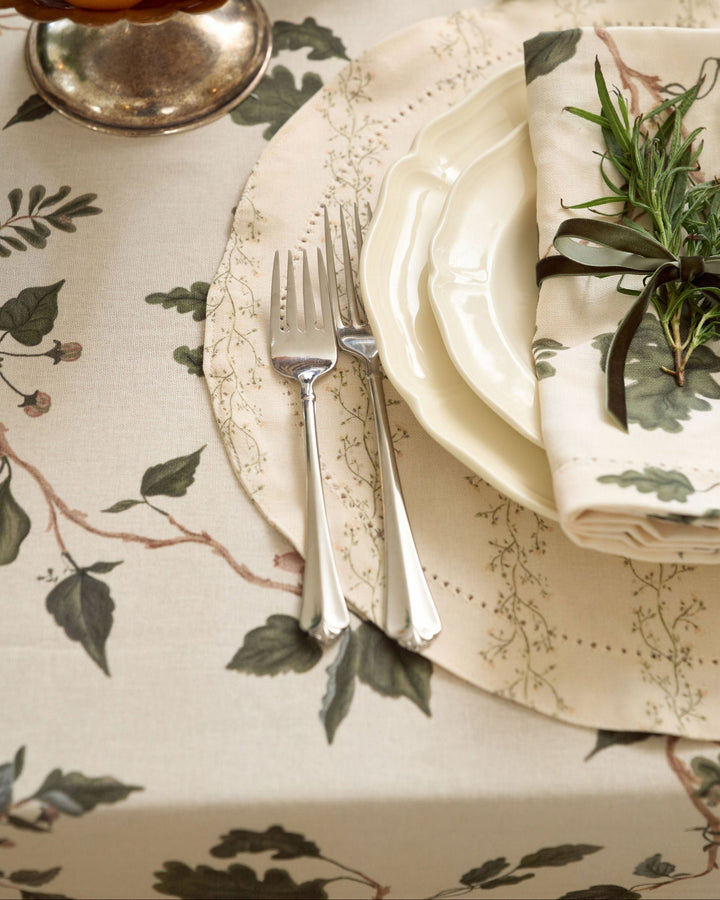 Classic English garden Christmas table with a cream botanical tablecloth, oak leaves, berries, taper candles, and a cut crystal centerpiece.