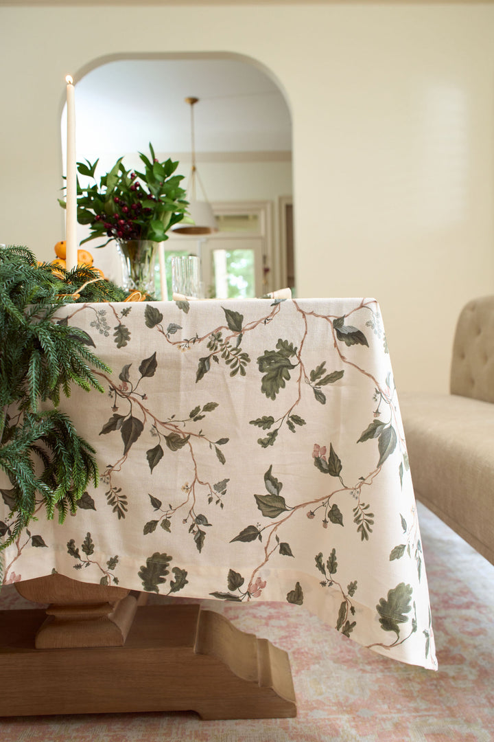 Botanical holiday table styled with an English countryside floral tablecloth, oak garden motifs, winter greenery, and elegant crystal glassware.