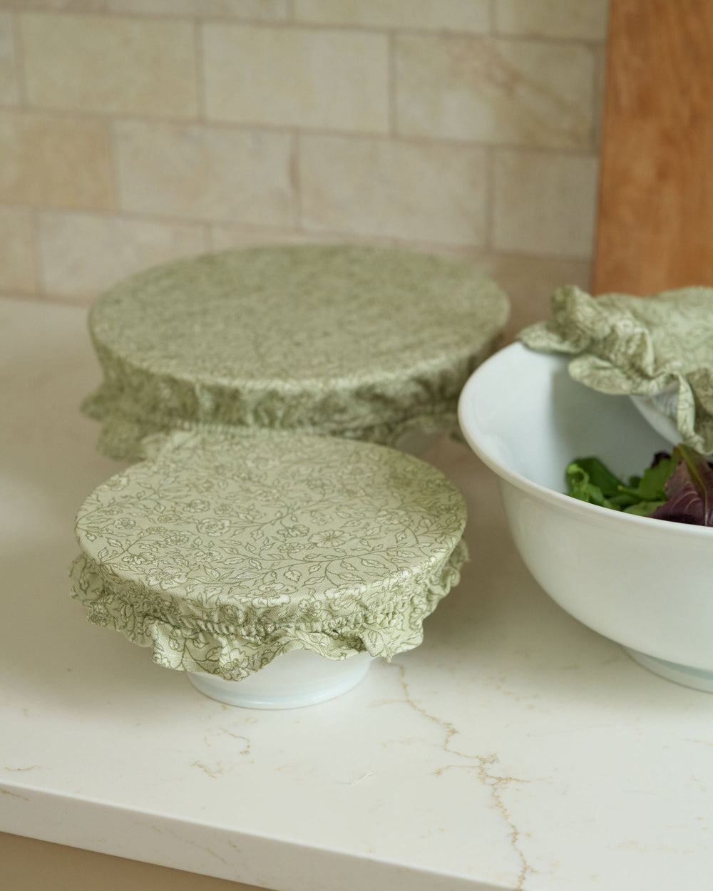 Reusable sage green botanical bowl covers made from breathable premium cotton with soft elastic edges and ruffle detailing, designed for mixing bowls, serving dishes, short-term food storage, meal prep, holiday baking, hostess gifts, housewarming gifts, and year-round kitchen organization.