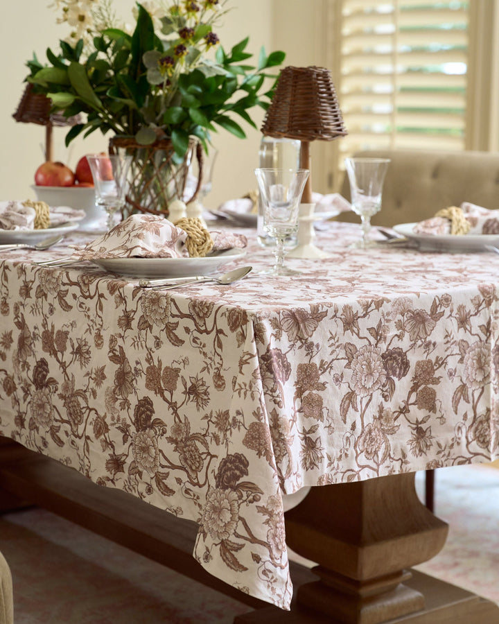 Brown floral cotton tablecloth with a hand-drawn botanical print, styled for an elegant fall table with classic dinnerware, warm seasonal accents, and layered linens.