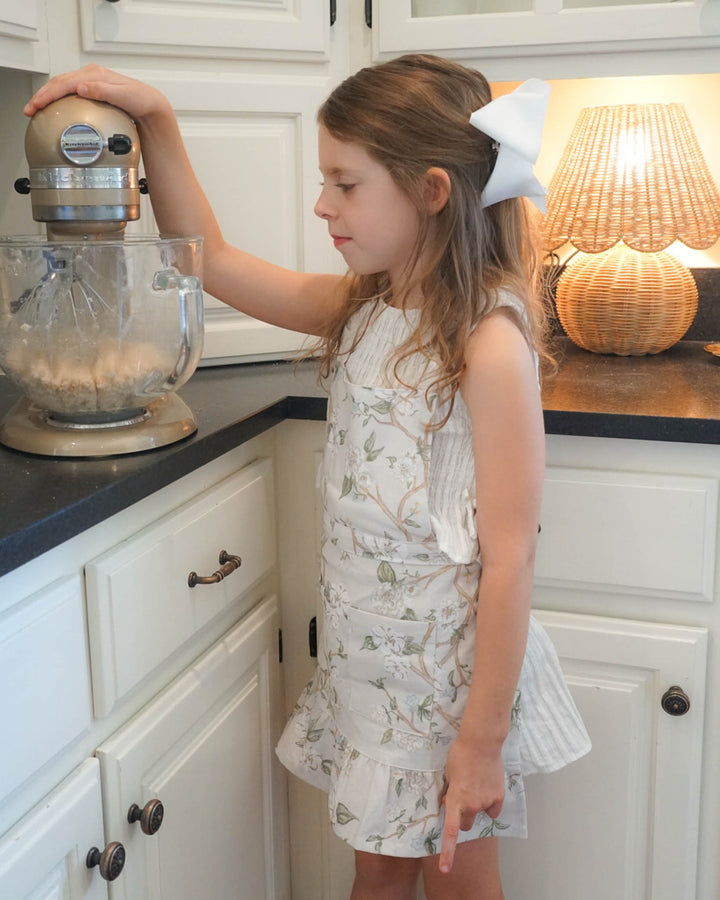 Camellia children’s apron with ruffle detail and pockets, perfect for young chefs and kitchen helpers.
