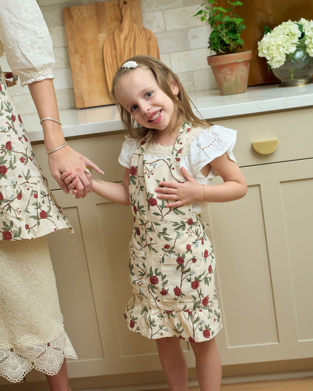 Red and green floral children’s apron for Christmas cookie baking, holiday crafts, and imaginative play. Made from premium cotton, it includes practical front pockets, adjustable ties, and a playful ruffle hem. Create a matching mommy-and-me apron set for festive family traditions in the kitchen. Personalize it with an embroidered initial or monogram.
