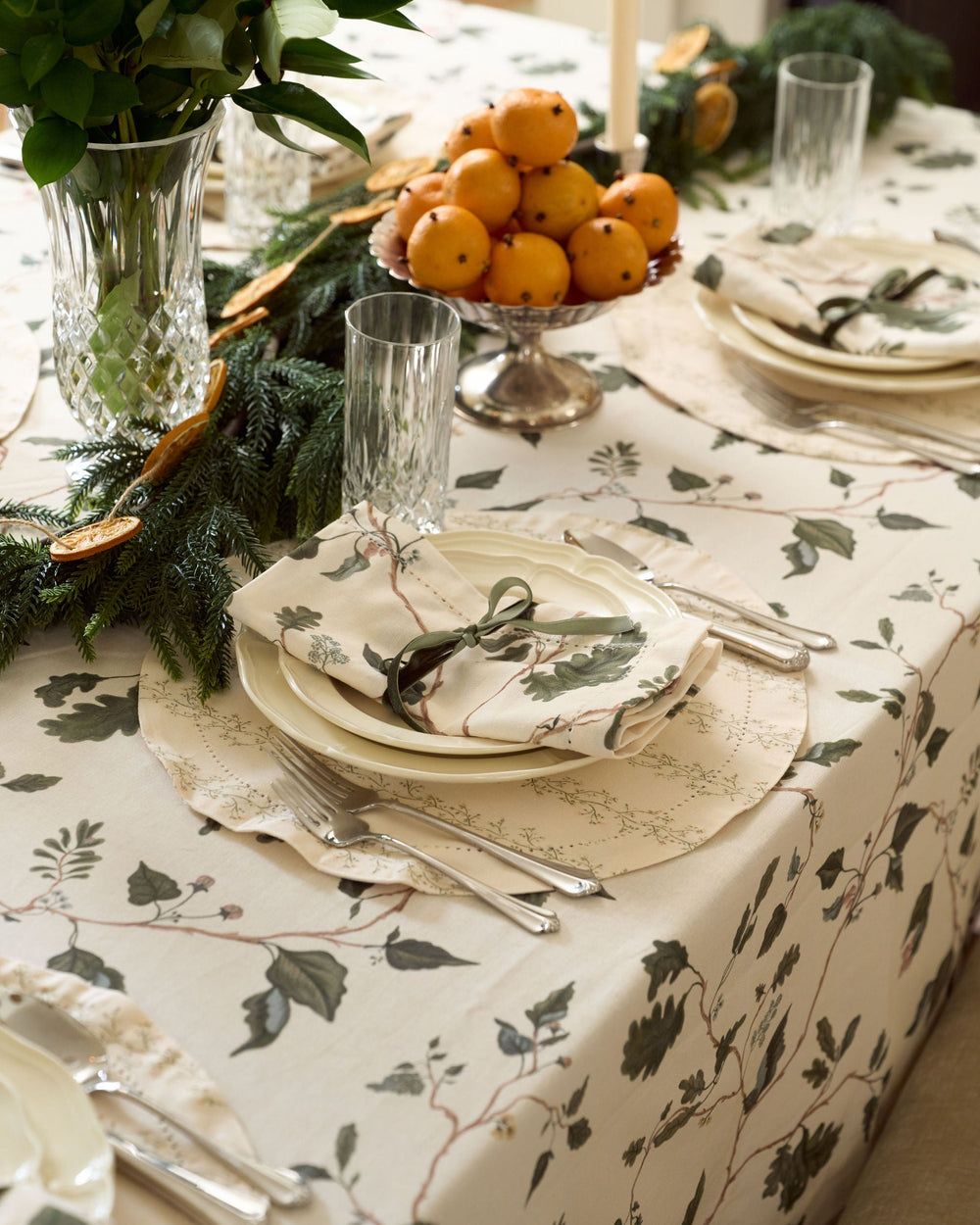 Neutral Christmas table linens featuring a cream botanical tablecloth, English countryside oak leaf print, evergreen garland, and crystal centerpiece.