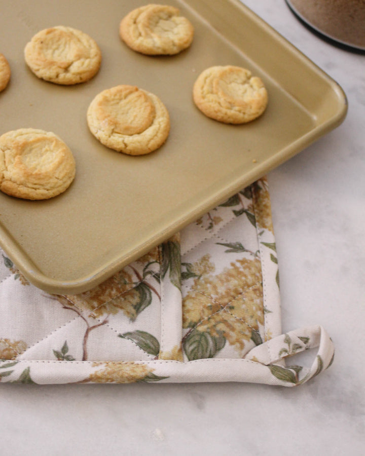 Elevate your spring hosting with these yellow botanical floral quilted hot pads. This set of two 8-inch square potholders is made from premium cotton, providing excellent heat insulation for hot pots and pans. Use them as decorative trivets on your dining table or as functional pot holders for lemon-themed baking. The intricate diamond quilting and bright floral pattern make them a beautiful Mother's Day or Easter gift. These charming yellow floral potholders bring joy to any kitchen.