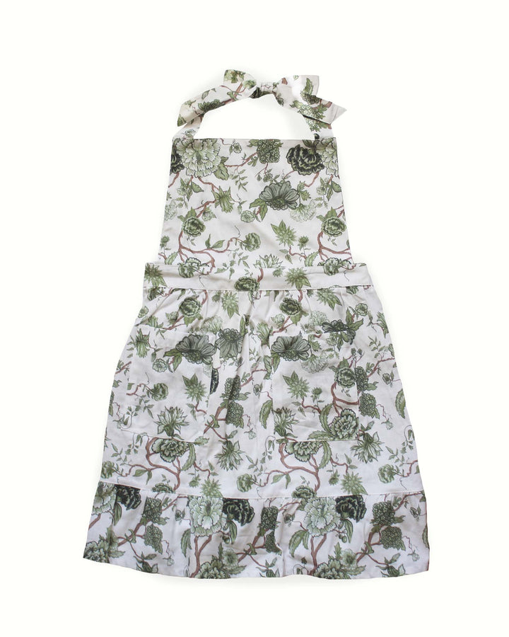 Hand-drawn floral green cotton apron with two front pockets, ruffle hem and adjustable ties, designed for home cooks, bakers, and kitchen hosting. Made with 100% cotton. 