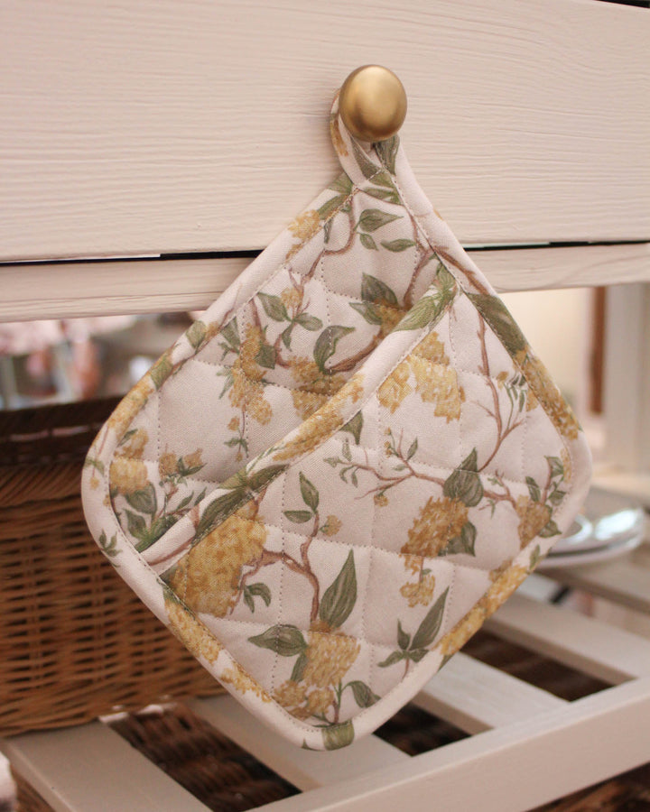 Durable quilted potholders in a vibrant yellow floral print, designed to handle the heat of a busy spring kitchen. This set of two 8-inch square hot pads features a thick insulated interior for maximum hand protection while handling baking sheets. The botanical meadow design is printed on high-quality cotton, offering a timeless aesthetic for farmhouse or modern kitchens. With a built-in hanging loop, these yellow floral hot pads are easy to display as part of your seasonal kitchen decor.