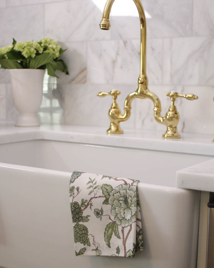 Cotton tea towel in green floral print, styled draped by the sink or hanging for a lived-in kitchen feel.