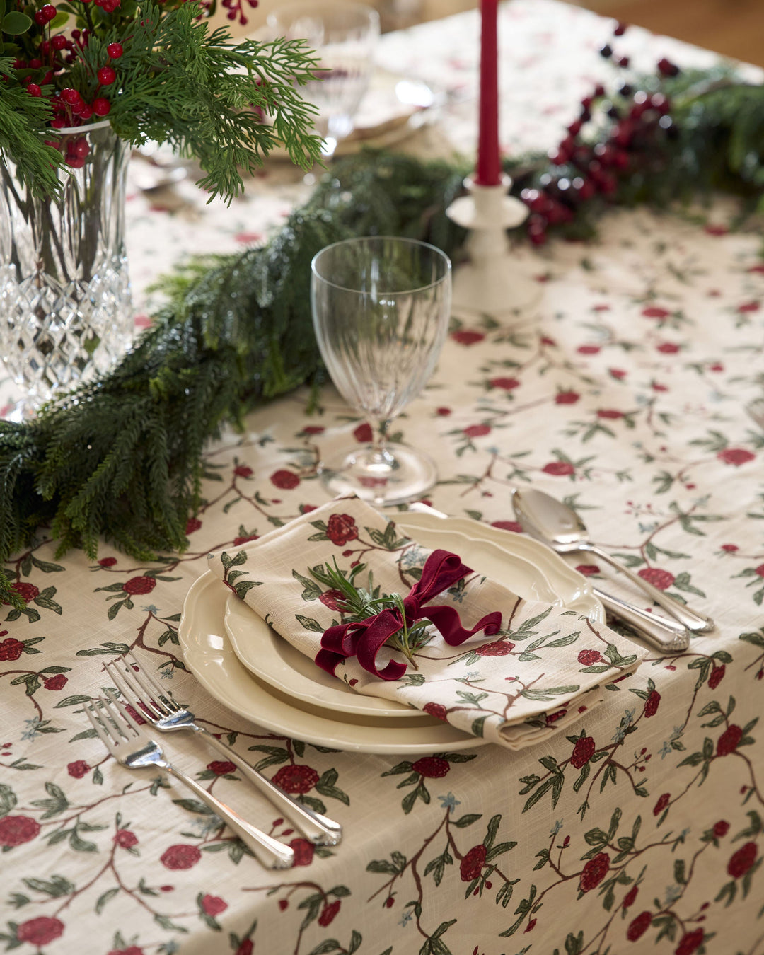 Elegant holiday tablescape featuring classic red and green table linens, layered dinnerware, seasonal greenery, and traditional Christmas accents.