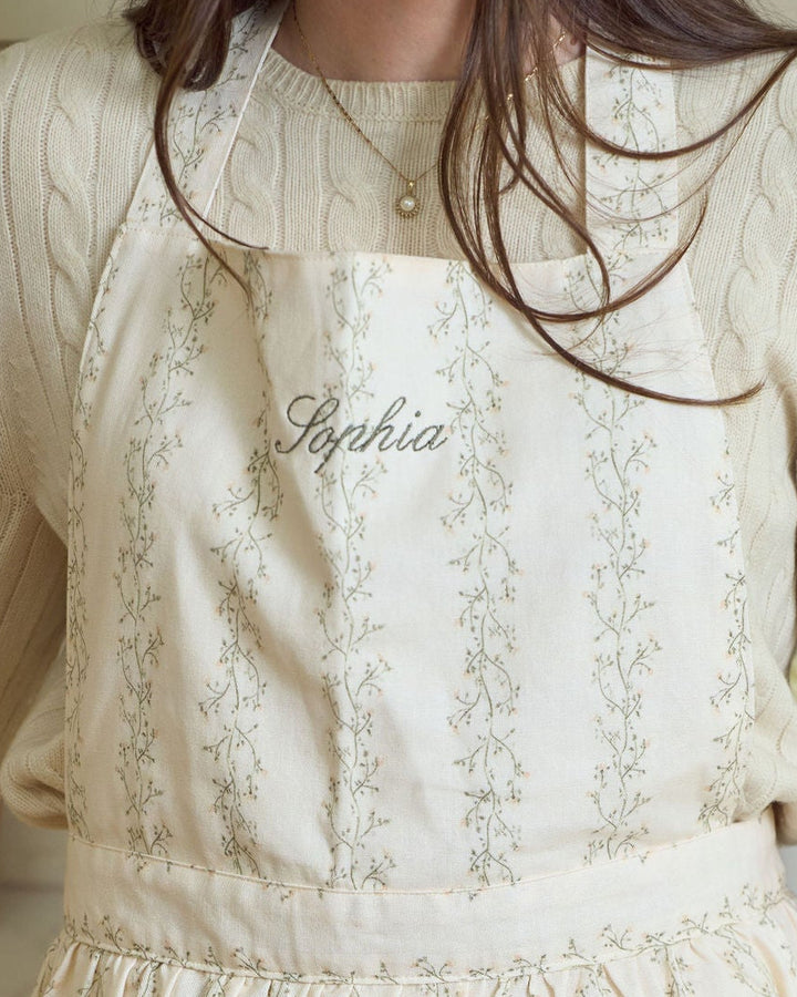 Personalized floral apron in premium cotton with a soft cream botanical stripe, practical pockets, feminine ruffle trim, and adjustable fit, perfect for monogrammed bridal shower gifts, housewarming gifts, hostess gifts, holiday baking, and year-round kitchen use.