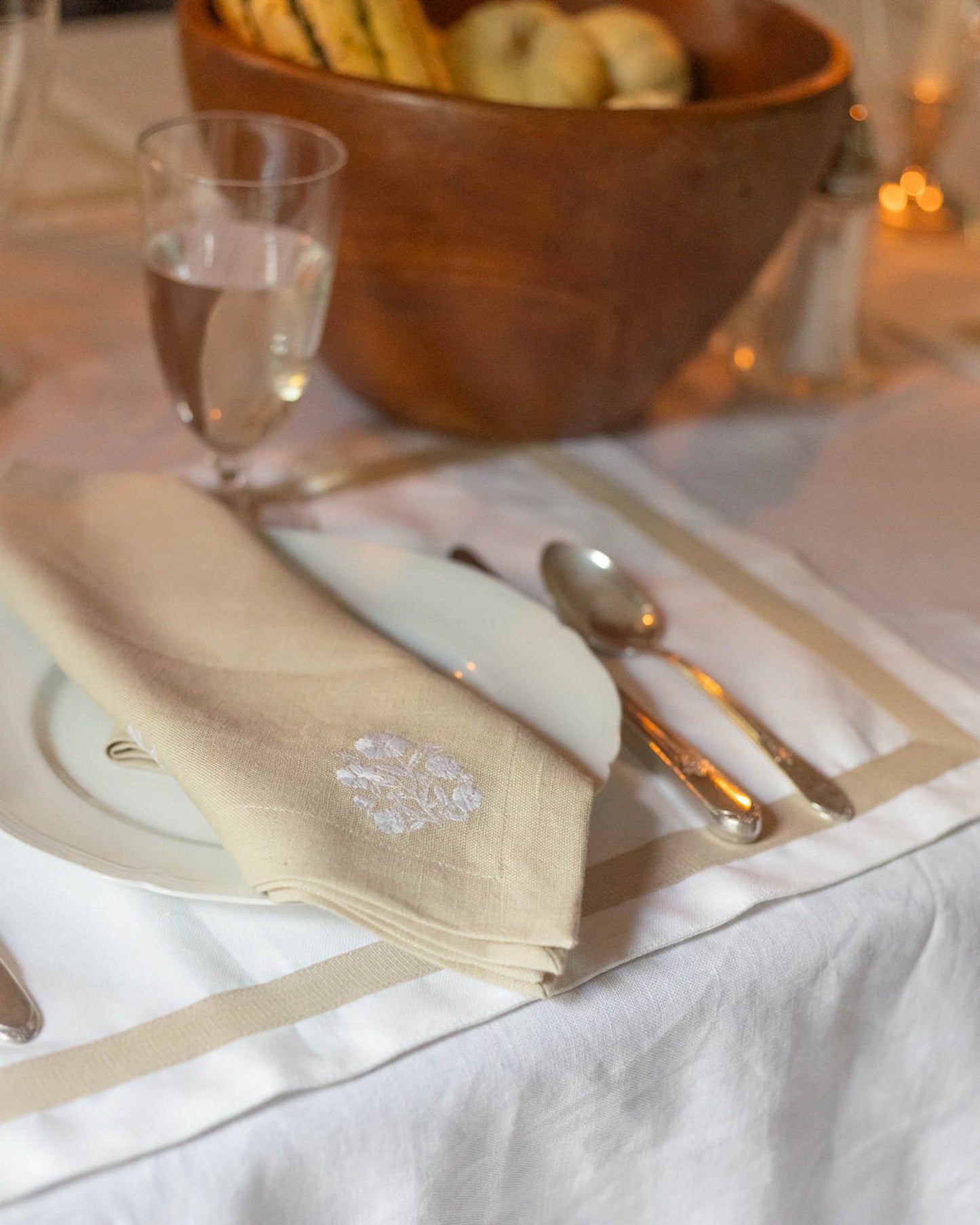 Dinner table setting with a beige napkin, silverware, and a wooden bowl in the background. Perfect for Thanksgiving tablescapes and Fall kitchen decor.