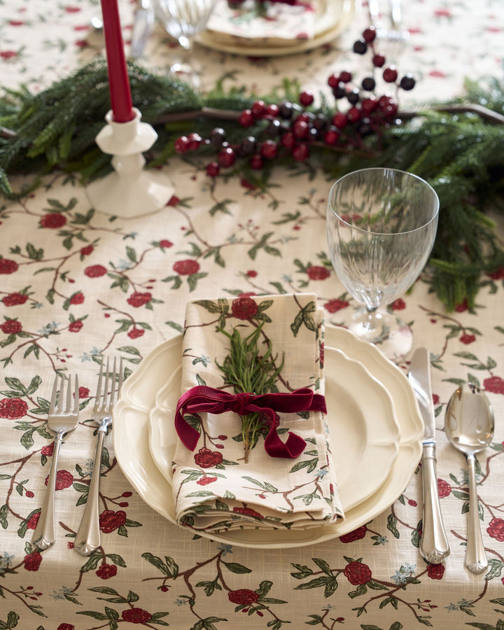Elegant Christmas dining table styled with red and green floral linens, matching napkins, seasonal greenery, and classic holiday place settings.