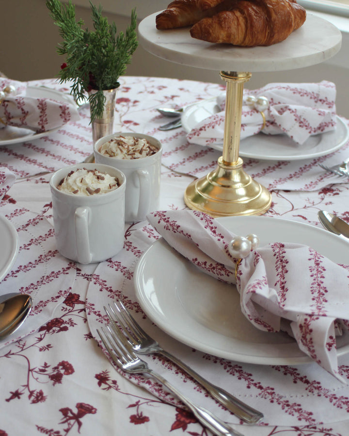 Red floral Christmas tablecloth and matching linens styled for an elegant holiday table setting.