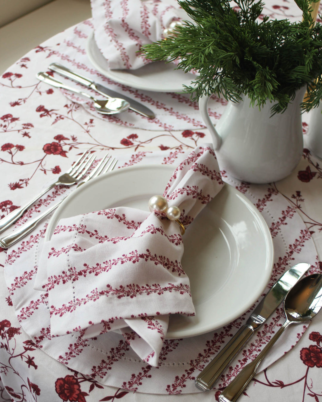 Elegant holiday tablescape featuring red floral table linens, layered place settings, and festive Christmas details.