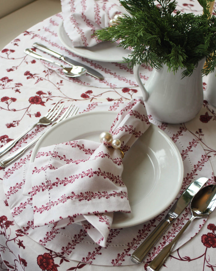 Elegant holiday tablescape featuring red floral table linens, layered place settings, and festive Christmas details.